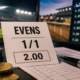 evens odds on betting slip in front of screen, with notepad and coins and odds screen next to it