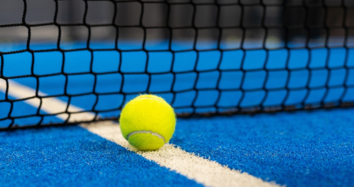 Tennis ball next to net on blue court